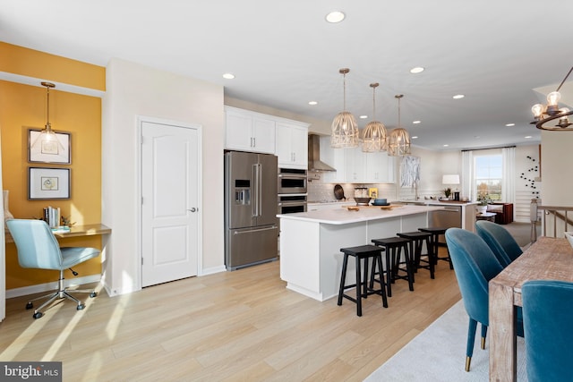 kitchen featuring white cabinetry, wall chimney range hood, appliances with stainless steel finishes, and hanging light fixtures