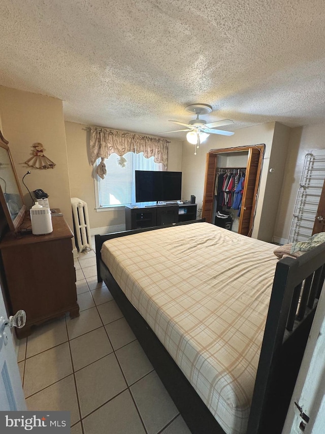 bedroom with ceiling fan, a textured ceiling, light tile patterned floors, radiator heating unit, and a closet