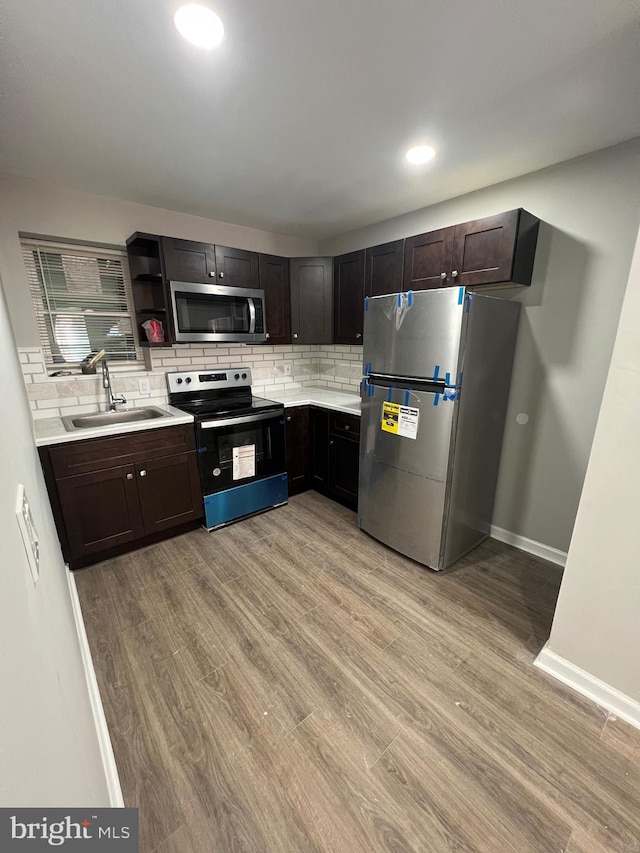 kitchen with appliances with stainless steel finishes, dark brown cabinetry, decorative backsplash, sink, and light hardwood / wood-style flooring