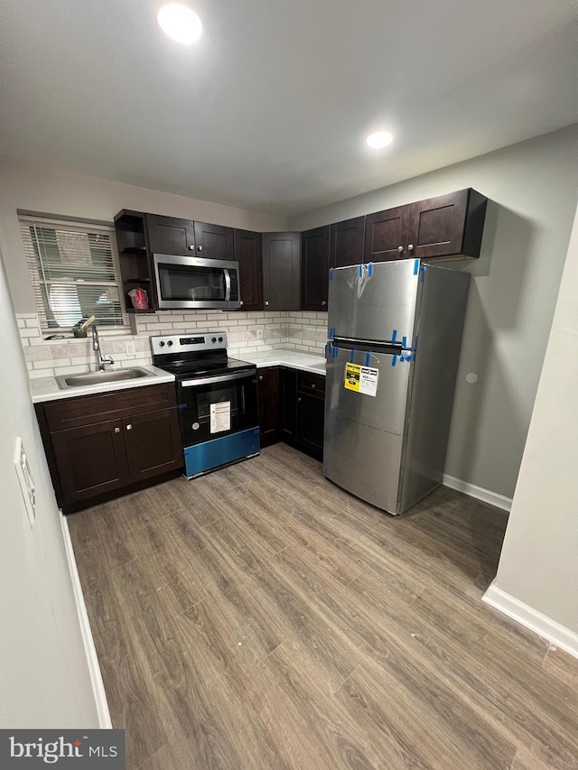 kitchen with appliances with stainless steel finishes, a sink, decorative backsplash, light countertops, and light wood-type flooring