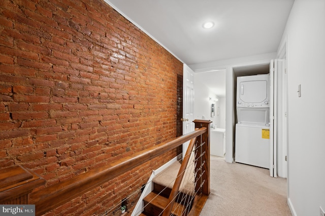 corridor featuring brick wall and stacked washer / drying machine