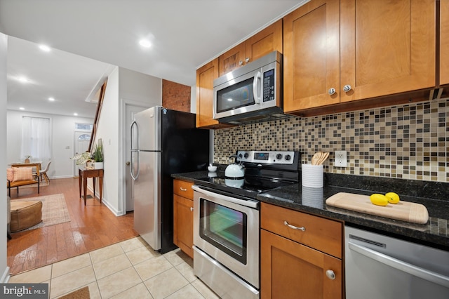 kitchen featuring light hardwood / wood-style flooring, tasteful backsplash, dark stone counters, and stainless steel appliances