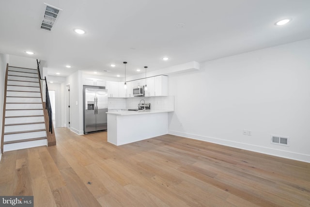 kitchen with stainless steel appliances, kitchen peninsula, decorative light fixtures, white cabinets, and light wood-type flooring