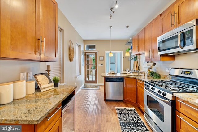 kitchen with light stone counters, light hardwood / wood-style flooring, pendant lighting, and appliances with stainless steel finishes