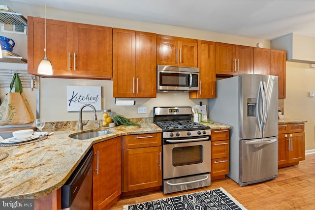 kitchen with hanging light fixtures, sink, light stone countertops, appliances with stainless steel finishes, and light hardwood / wood-style floors