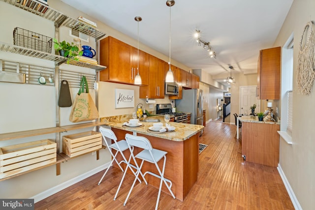 kitchen featuring stainless steel appliances, light stone counters, kitchen peninsula, pendant lighting, and light hardwood / wood-style floors