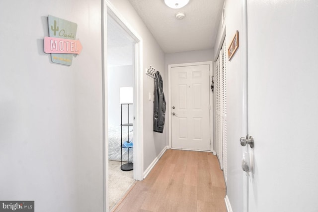 hallway with light wood-type flooring and a textured ceiling