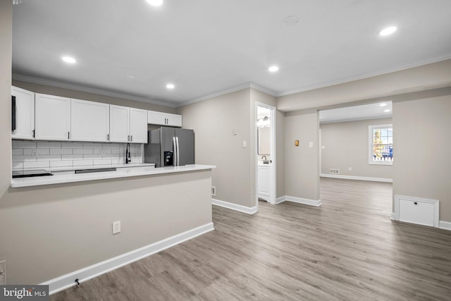 kitchen with light hardwood / wood-style floors, white cabinets, crown molding, backsplash, and stainless steel fridge