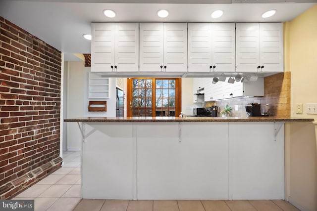 kitchen with brick wall, stainless steel fridge, white cabinets, and kitchen peninsula