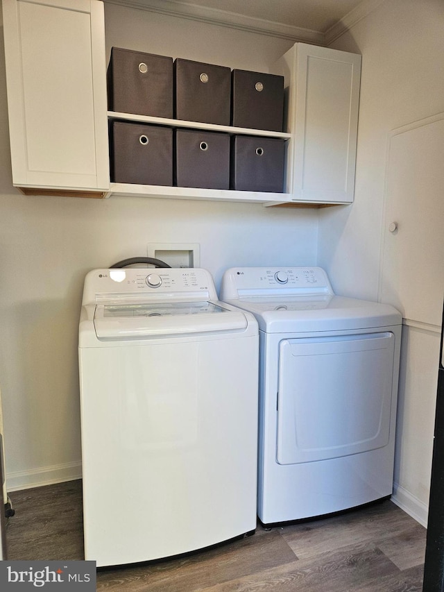 laundry room featuring dark wood-type flooring, washing machine and dryer, cabinets, and ornamental molding