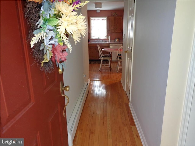 hallway with a baseboard heating unit, light hardwood / wood-style floors, and sink