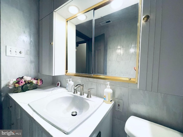 bathroom with toilet, vanity, and tile walls