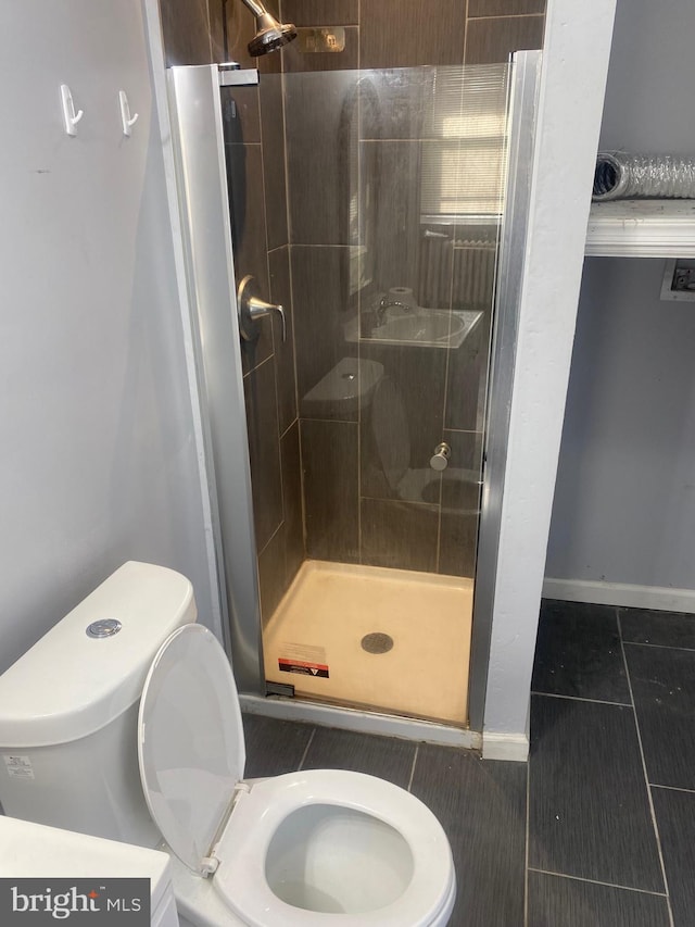 bathroom featuring a shower with shower door, tile patterned flooring, and toilet