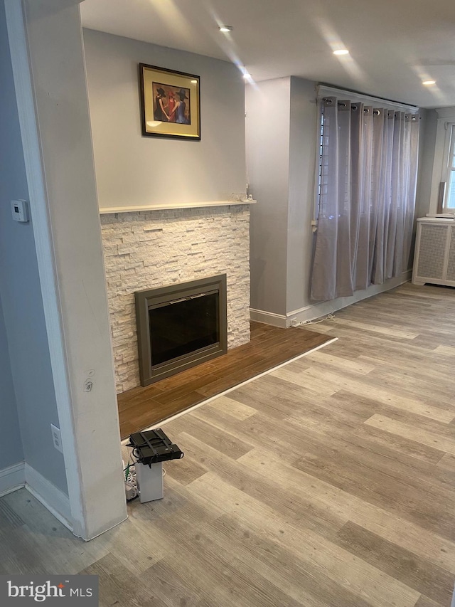 unfurnished living room featuring a stone fireplace, radiator, and hardwood / wood-style flooring