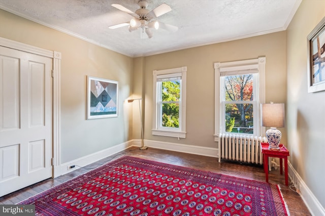 living area featuring radiator, dark wood-type flooring, ceiling fan, ornamental molding, and a textured ceiling