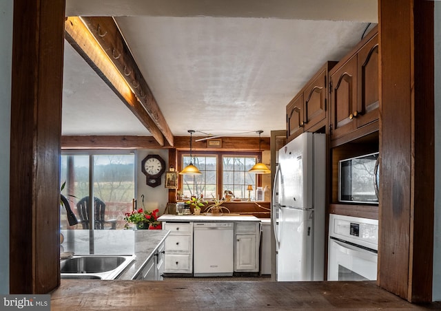 kitchen featuring white appliances, a sink, healthy amount of natural light, hanging light fixtures, and beam ceiling