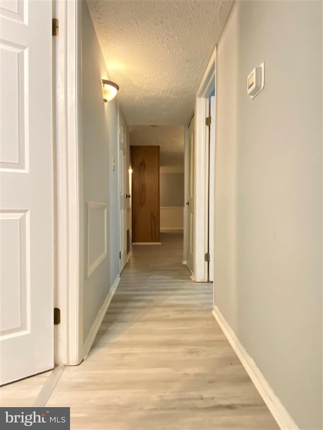 hallway with a textured ceiling and light wood-type flooring