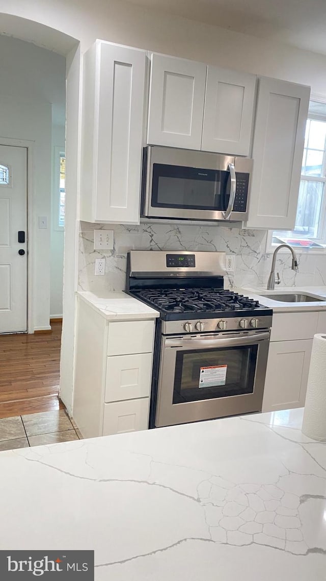 kitchen featuring white cabinets, backsplash, stainless steel appliances, and light hardwood / wood-style flooring