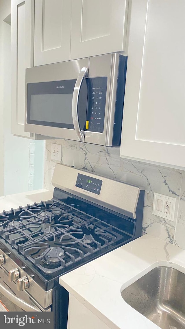 details with stainless steel appliances, light stone counters, tasteful backsplash, and white cabinetry