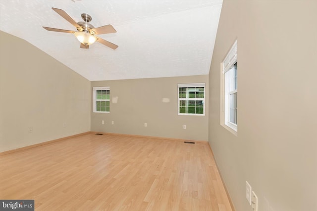 empty room with light wood-type flooring, a textured ceiling, and vaulted ceiling