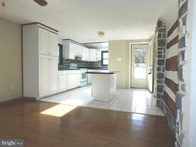 kitchen with backsplash, electric stove, light hardwood / wood-style flooring, a kitchen island, and white cabinetry