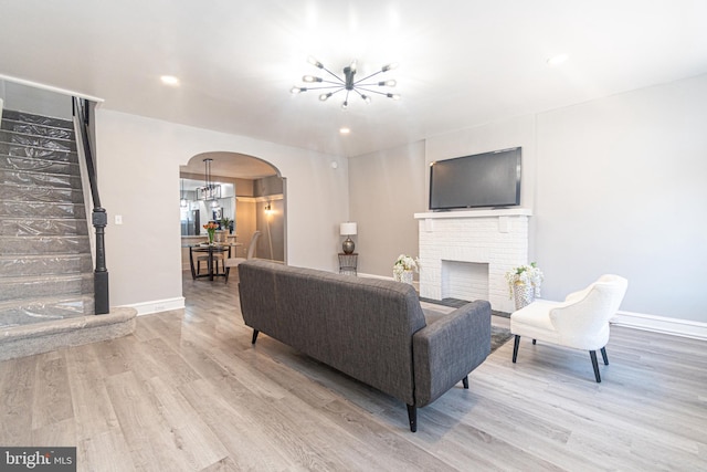 living room featuring a brick fireplace, light hardwood / wood-style floors, and a notable chandelier