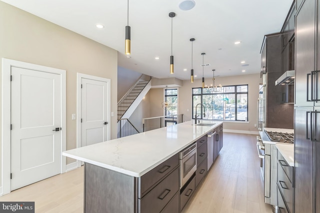 kitchen with appliances with stainless steel finishes, light wood-type flooring, a spacious island, sink, and pendant lighting