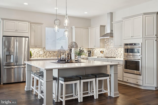 kitchen featuring stainless steel appliances, a kitchen island, wall chimney range hood, and dark hardwood / wood-style flooring