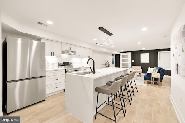 kitchen featuring stainless steel appliances, white cabinets, an island with sink, and light wood-type flooring