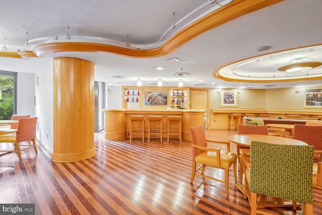 dining room featuring bar, wood-type flooring, a raised ceiling, and decorative columns