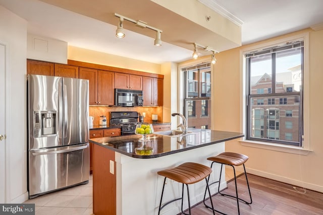 kitchen with light hardwood / wood-style floors, black appliances, a breakfast bar area, tasteful backsplash, and an island with sink