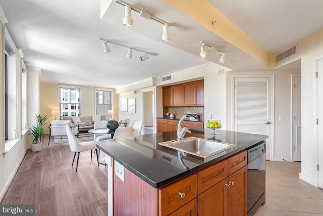 kitchen with light hardwood / wood-style floors, sink, backsplash, an island with sink, and black dishwasher