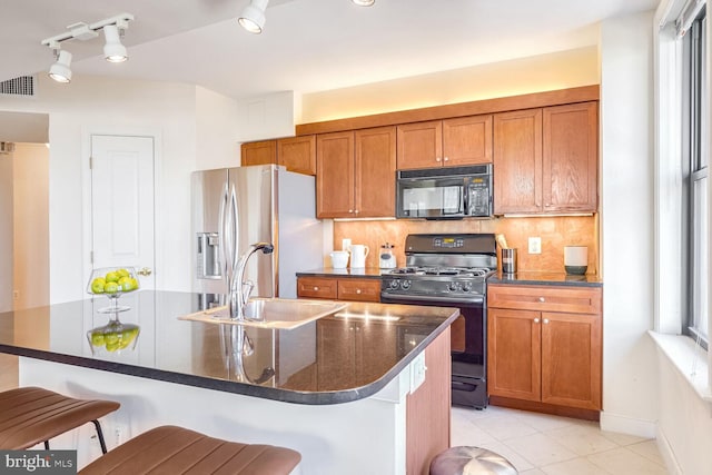 kitchen featuring sink, black appliances, a kitchen bar, rail lighting, and a kitchen island with sink