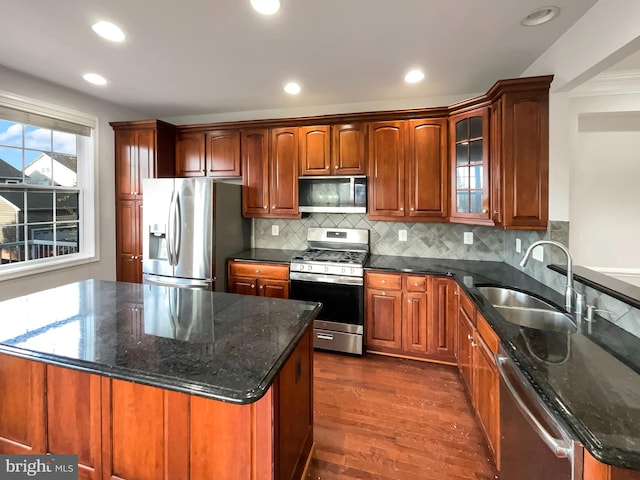 kitchen with sink, appliances with stainless steel finishes, dark stone counters, a center island, and dark wood-type flooring