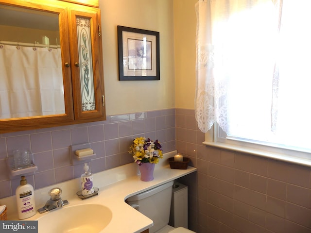 bathroom with toilet, vanity, and tile walls