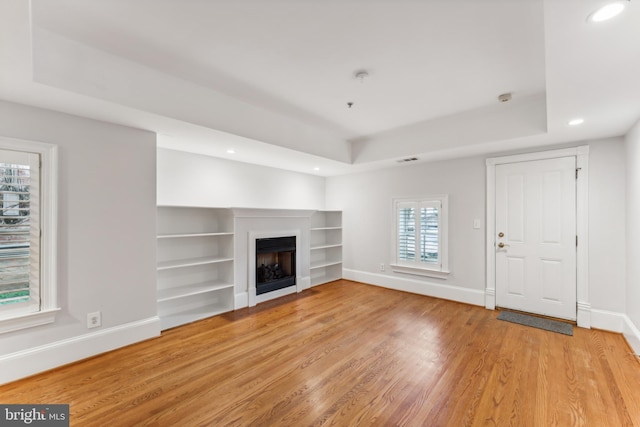 unfurnished living room featuring light hardwood / wood-style floors and a raised ceiling