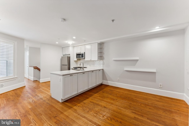 kitchen featuring white cabinetry, light wood-type flooring, stainless steel appliances, and backsplash