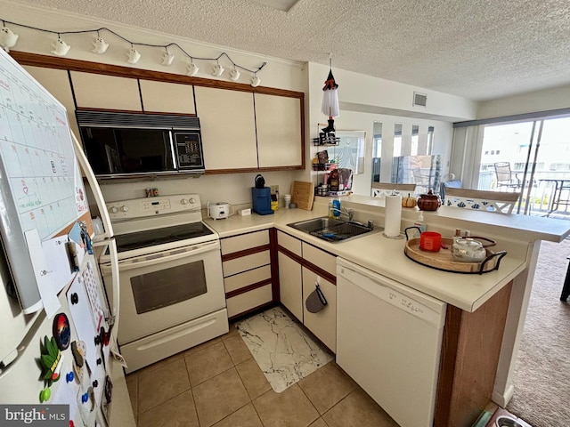 kitchen with a peninsula, white appliances, light countertops, and a sink