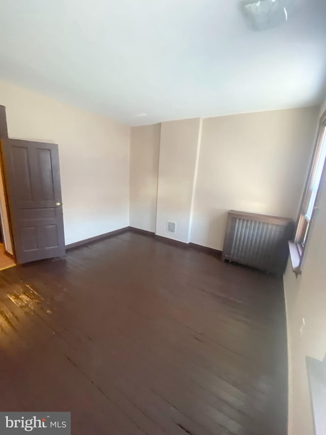 spare room featuring dark wood-type flooring and radiator