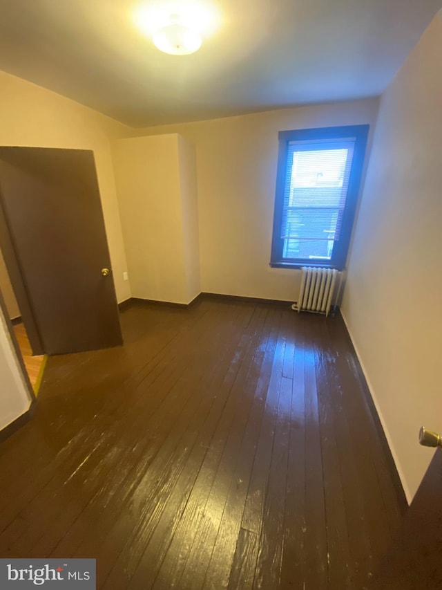 spare room featuring radiator heating unit and dark hardwood / wood-style floors