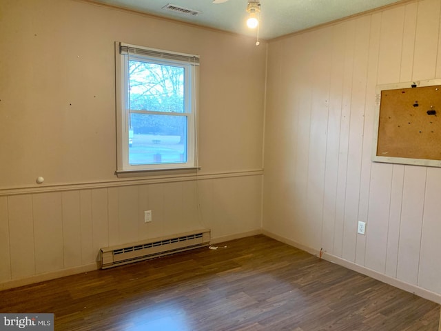 spare room with wooden walls, ornamental molding, dark hardwood / wood-style floors, and a baseboard heating unit