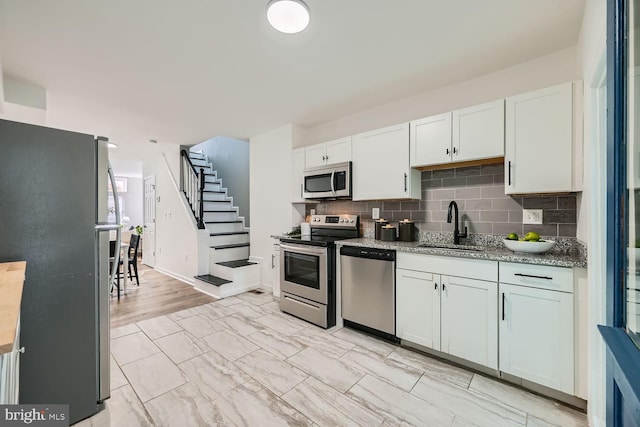 kitchen with tasteful backsplash, light stone counters, appliances with stainless steel finishes, sink, and white cabinets