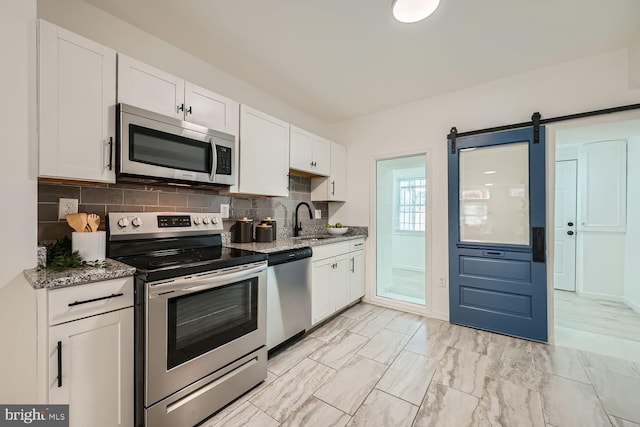 kitchen with stainless steel appliances, sink, backsplash, white cabinets, and a barn door