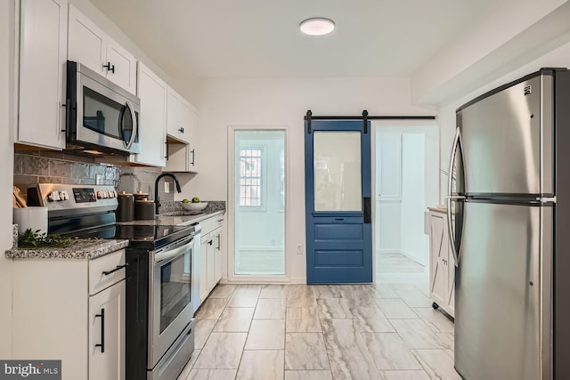 kitchen featuring a barn door, white cabinets, backsplash, and appliances with stainless steel finishes