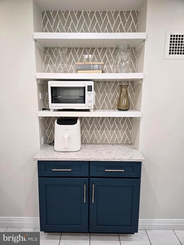 bar with blue cabinetry, light tile patterned floors, and backsplash