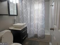 full bathroom featuring toilet, shower / tub combo with curtain, and vanity