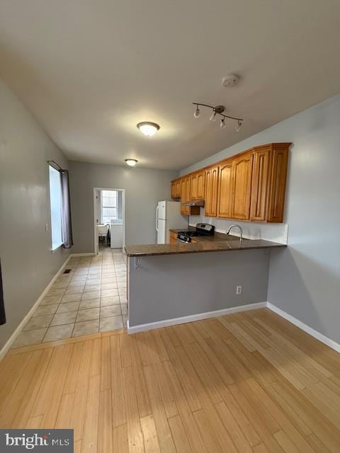 kitchen with white refrigerator, kitchen peninsula, stainless steel range oven, sink, and light wood-type flooring