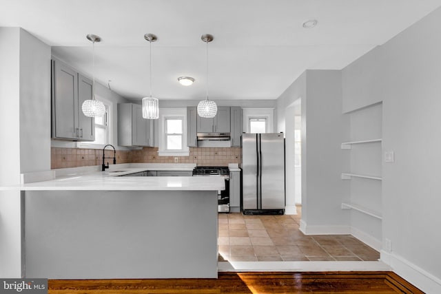 kitchen featuring kitchen peninsula, backsplash, gray cabinetry, stainless steel appliances, and light hardwood / wood-style flooring