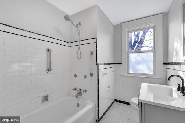 full bathroom with vanity, tile patterned floors, tiled shower / bath combo, toilet, and tile walls