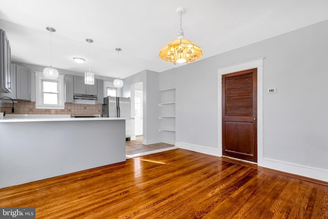 kitchen featuring tasteful backsplash, light hardwood / wood-style flooring, gray cabinets, stainless steel refrigerator, and hanging light fixtures